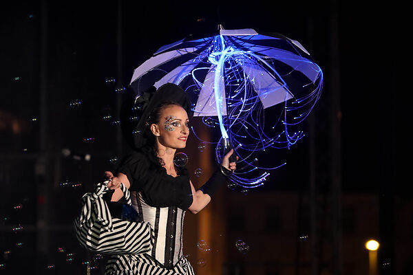 Auf dem Bild ist eine verkleidete Frau mit einem Regenschirm in der Hand zu sehen. Um sie herum fliegen Seifenblasen.