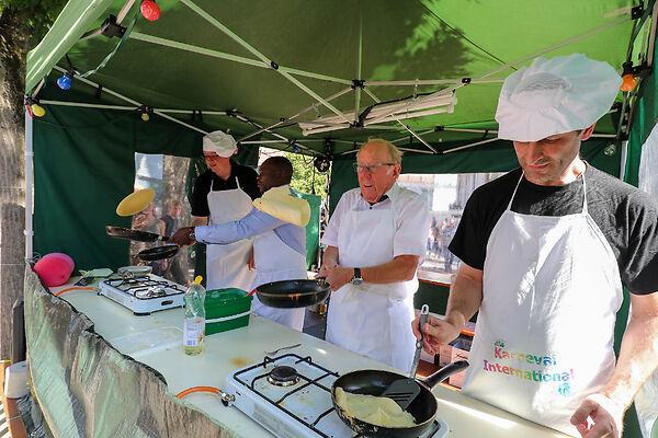 Auf dem Bild sind Männer zu sehen, die hinter einem Stand Pfannkuchen backen.