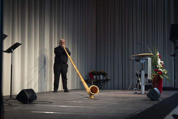 Auf dem Bild ist ein Mann zu sehen, der auf einem Alphorn spielt.