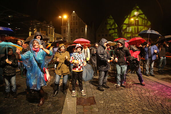 Auf dem Bild sind Besucher*innen der Reichsstädter Tage zu sehen, die sich mit Regenmänteln und Regenschirmen vor dem Regen schützen.