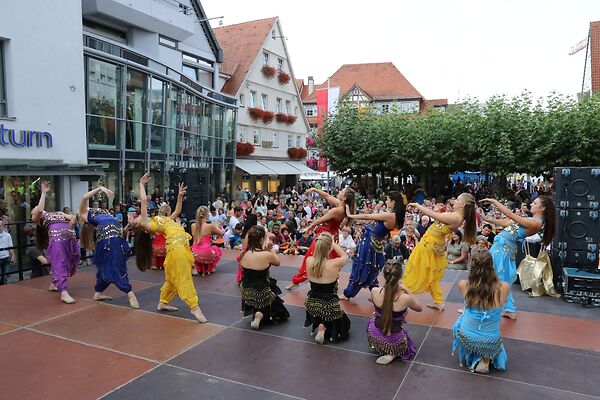 Auf dem Bild sind tanzende Frauen in bunten Gewändern auf einer Bühne zu sehen.