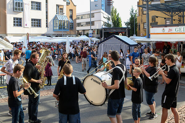 Auf dem Bild ist eine Gruppe zu sehen, die auf dem Gmünder Torplatz mit Blasinstrumenten auftritt.