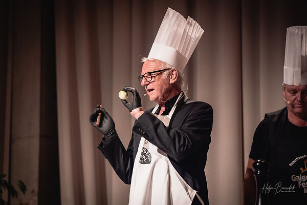 Auf dem Bild ist ein Mann mit Kochmütze und einer Zwiebel in der Hand zu sehen.