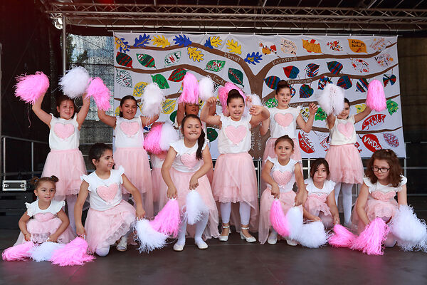 Auf dem Bild sind Kinder in rosaroten Kostümen zu sehen, die auf einer Bühne tanzen.