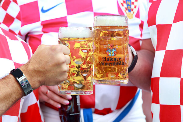 Auf dem Bild sind Menschen in Fußball-Trikots zu sehen, die gefüllte Bierkrüge in den Händen halten.