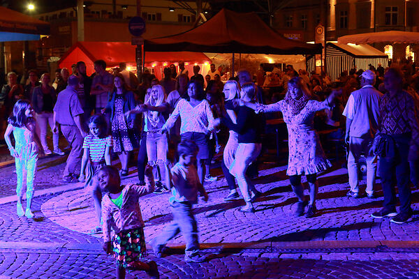 Auf dem Bild sind Personen zu sehen, die in der Nacht im Scheinwerferlicht tanzen.