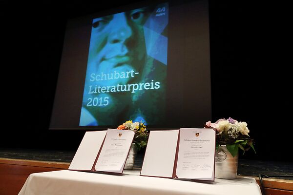 Auf dem Bild sind beide Urkunden des Schubart-Literaturpreises zu sehen, die auf einem Tisch auf einer Bühne ausgestellt sind.