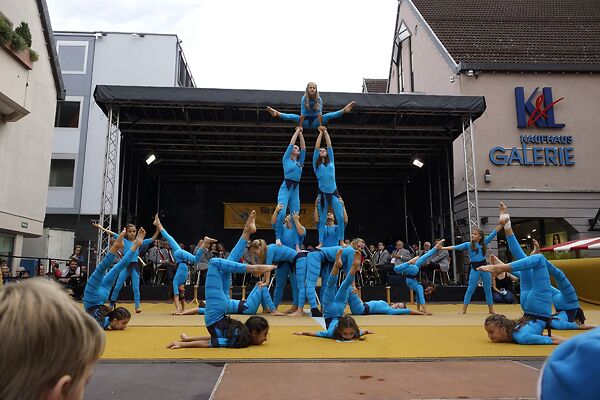 Auf dem Bild sind turnende Akrobatinnen und Akrobaten auf einer Bühne zu sehen.