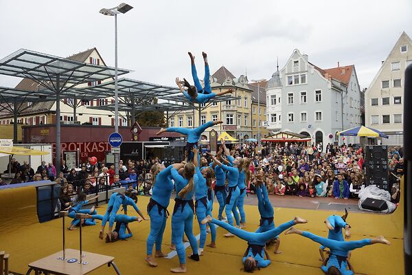 Auf dem Bild sind turnende Akrobatinnen und Akrobaten auf einer Bühne zu sehen.