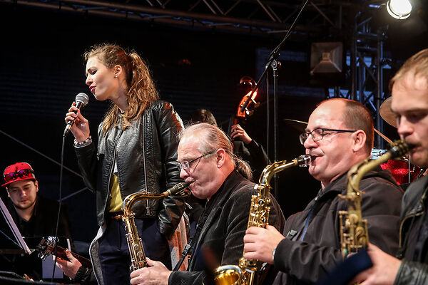 Auf dem Bild ist eine Sängerin und mehrere auf Saxophonen musizierende Herren zu sehen.