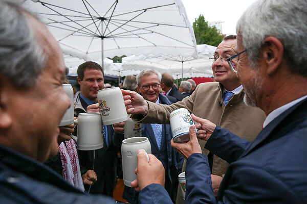 Auf dem Bild sind Herren zu sehen, die mit Bierkrügen anstoßen.