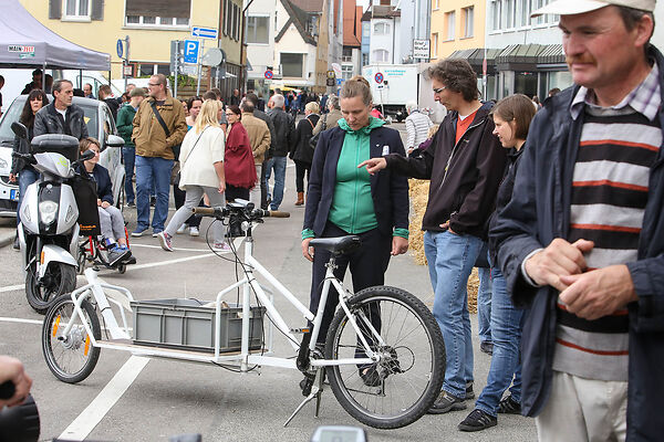 Auf dem Bild ist ein Lastenfahrrad zu sehen. Neben dem Lastenfahrrad stehen Menschen, die sich darüber unterhalten.