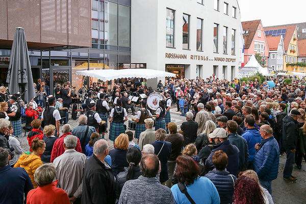 Auf dem Bild ist eine Menschenmenge zu sehen, die sich um in schottischen Gewänder gekleidete Musikanten versammelt haben. 