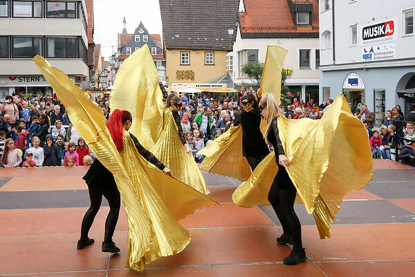 Auf dem Bild sind  drei tanzende Frauen in goldenen Gewändern auf einer Bühne zu sehen.