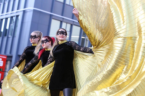 Auf dem Bild sind in schwarz-goldenen Gewändern gekleidete Frauen zu sehen, die auf einer Bühne tanzen.