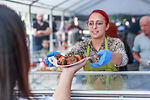 Auf dem Bild ist eine Frau, die Essen an einen Gast überreicht zu sehen.