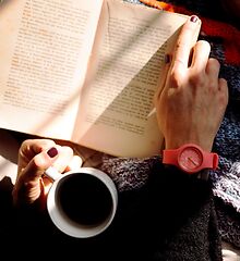 Auf dem Bild ist ein Buch, eine Kaffeetasse und eine Hand zu sehen.